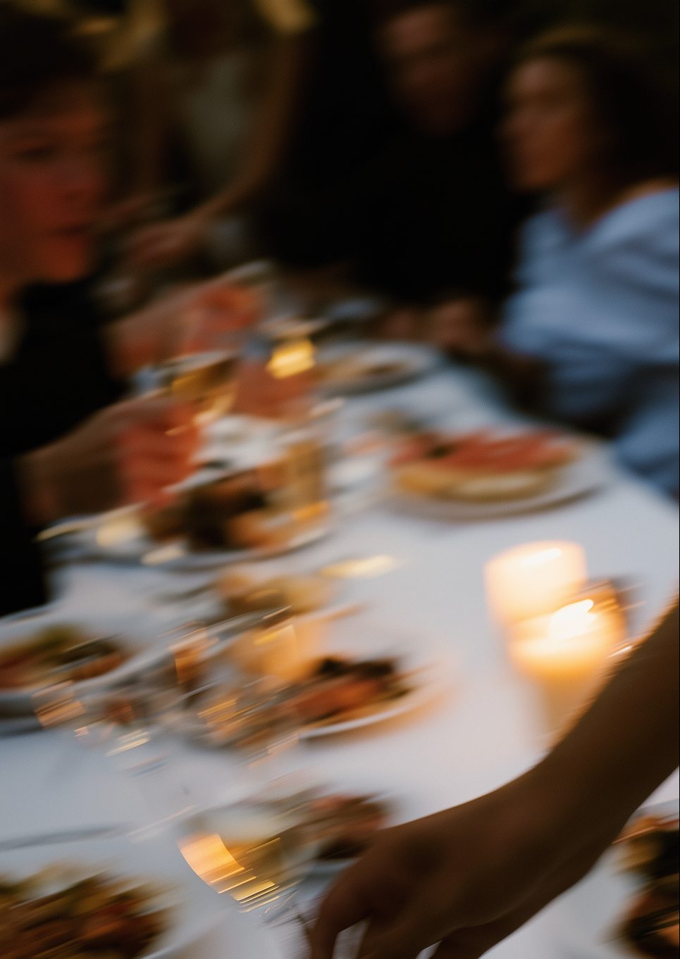A long candlelit dinner table, friends passing plates